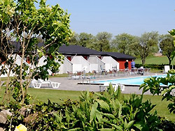 Bornholm: Folkemøde overnatning Sommerhus, Feriehus, Hotel, Pension - Ferielejlighed beliggende i det smukt kuperede landskab uden for Åkirkeby på Bornholm. Flot lejlighed i udkanten af hyggelige Åkirkeby med butikker, restauranter m.m. Lejligheden er en del af feriestedet Dams på Bakken, som bl.a. byder på stor udendørs swimmingpool med lav ende, stor trampolin, gynger og fodboldbane. Lejligheden har en hyggelig opholdsstue med TV/DVD og radio/cd. Åben køkkenafdeling med bl.a. miniovn, køleskab, fryser, elkomfur (2 plader), emhætte og spiseplads. Badeværelse med DU/WC og gulvvarme. To værelser. Udgang til egen terrasse med markise, havemøbler og grill. Kun 10 m til poolen. Lige ved siden af ligger oplevelsescenteret NaturBornholm. 4,5 km. væk finder man dejlige sandstrande. Fine muligheder for vandreture samt leg og boldspil lige uden for døren. Røgfri lejlighed og ingen husdyr. Bornholm: Folkemøde overnatning Sommerhus, Feriehus, Hotel, Pension - Dams på Bakken - dør 8